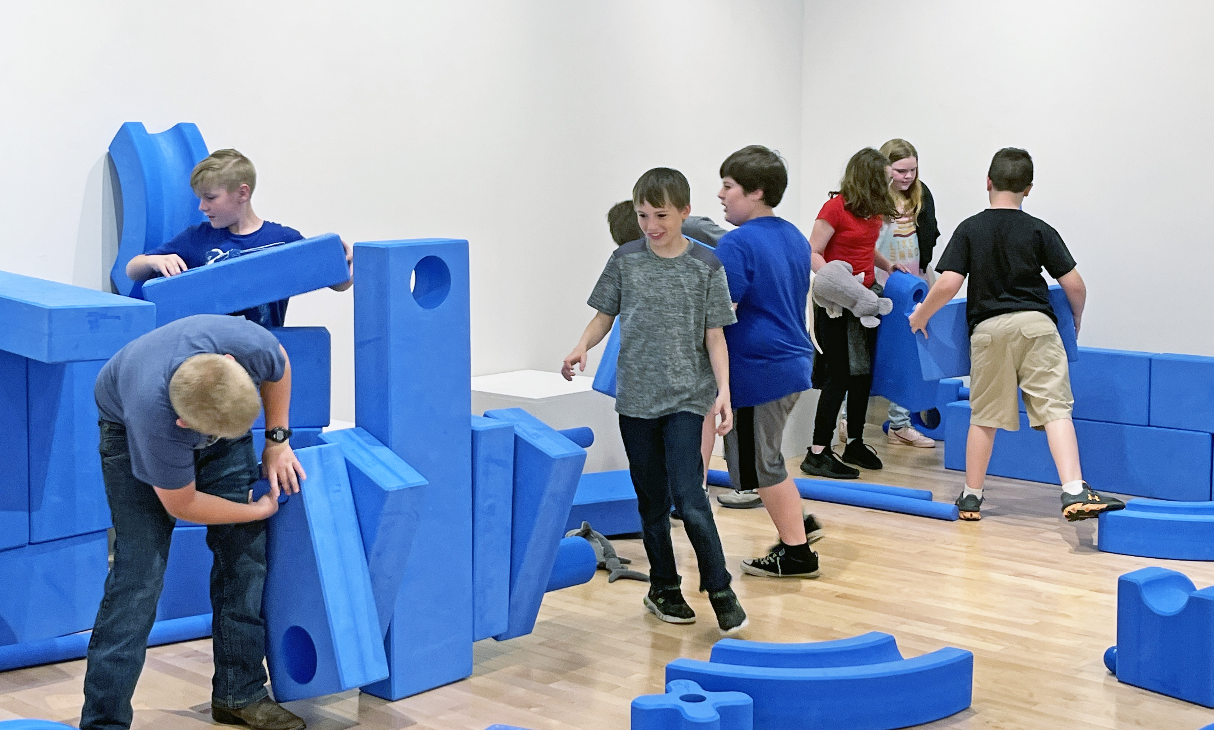 Kids play in a gallery with large blue blocks