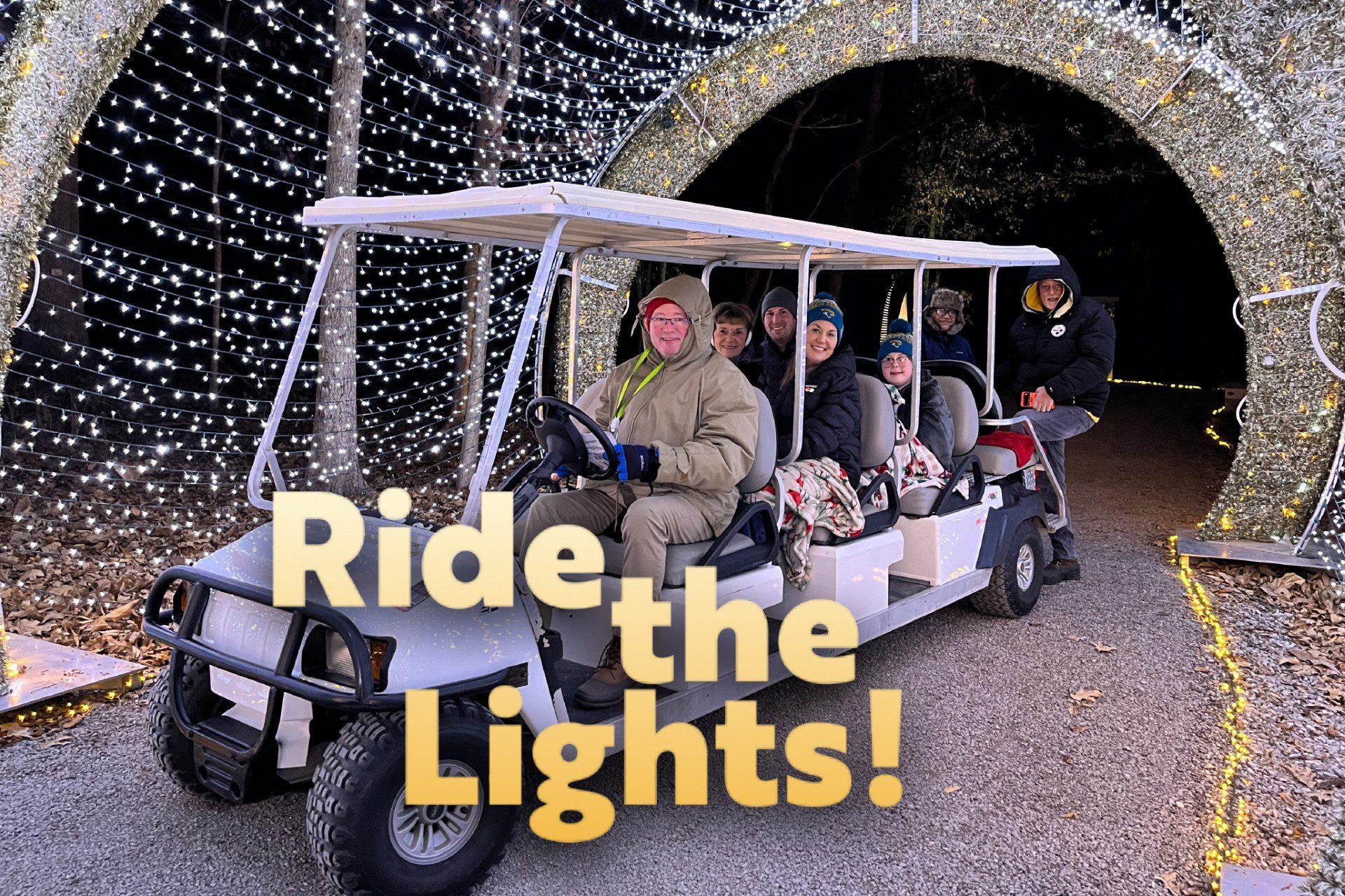 A group rides a golf cart through a Holiday Lights display